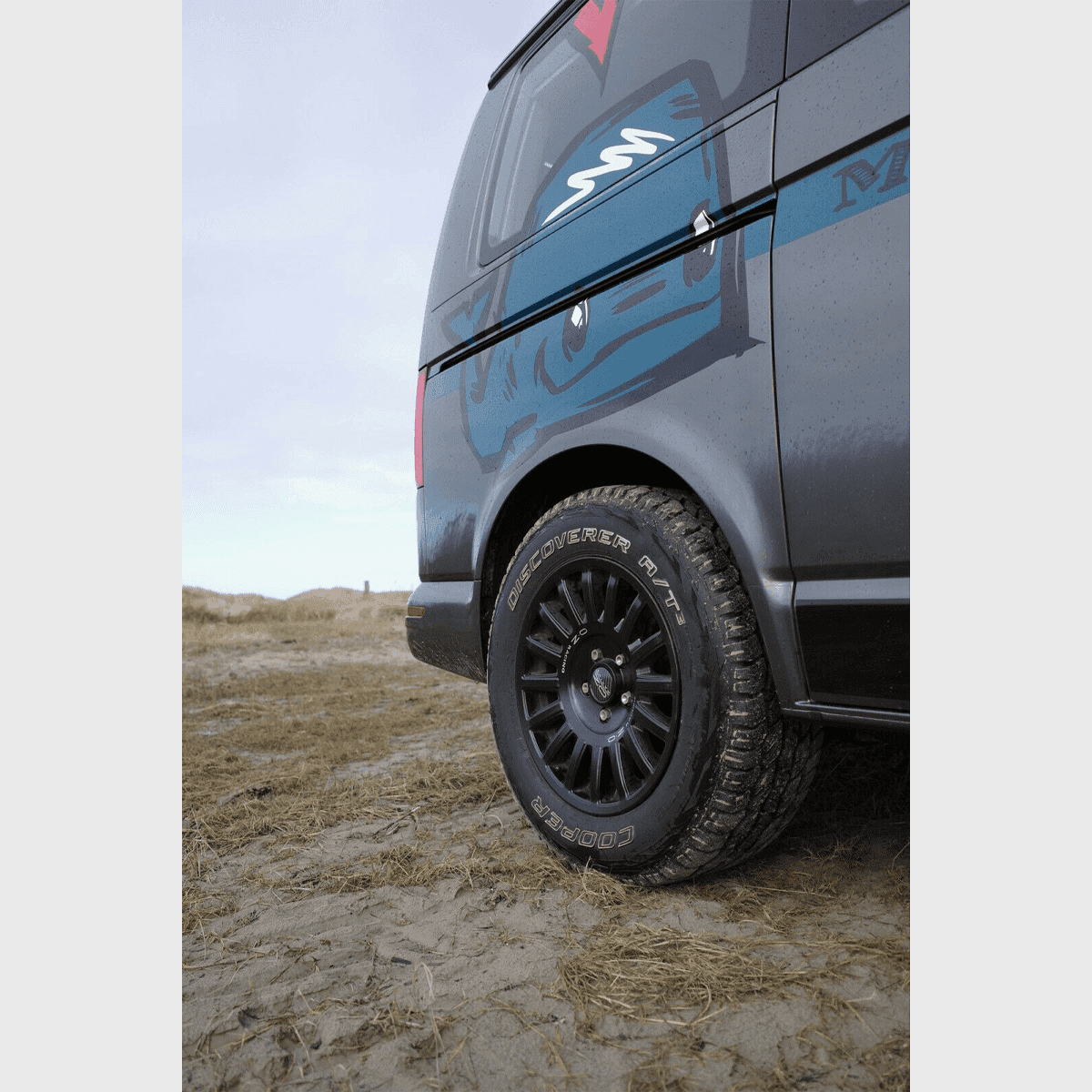 OZ Rally Raid Offroad-Felge am VW T5-T6.1 auf sandigem Gelände, seitliche Fahrzeugnahaufnahme mit Fokus auf den Reifen.