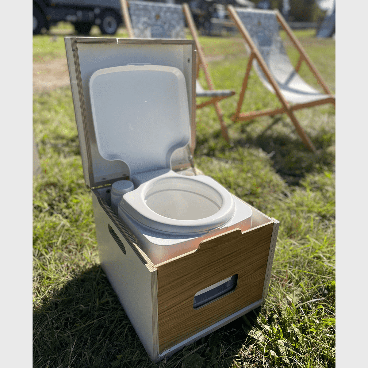 Moby PottiBOX für Porta Potti 335 in Holzkiste auf Wiese, umgeben von Campingstühlen, perfekt für Outdoor-Erlebnisse.