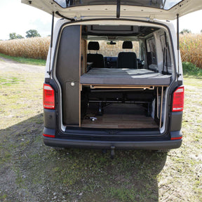 Wohnmobil mit offenem Heck, zeigt ein ausgeklapptes Bettsystem mit Vanmade Matratze in einem VW T5-T6.1, geparkt im Freien.