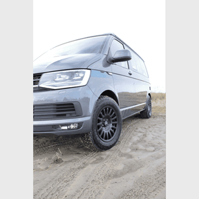 Grau-metallicfarbener VW T5 auf sandigem Untergrund mit OZ Rally Raid Offroad Felgen, Frontalansicht von rechts.