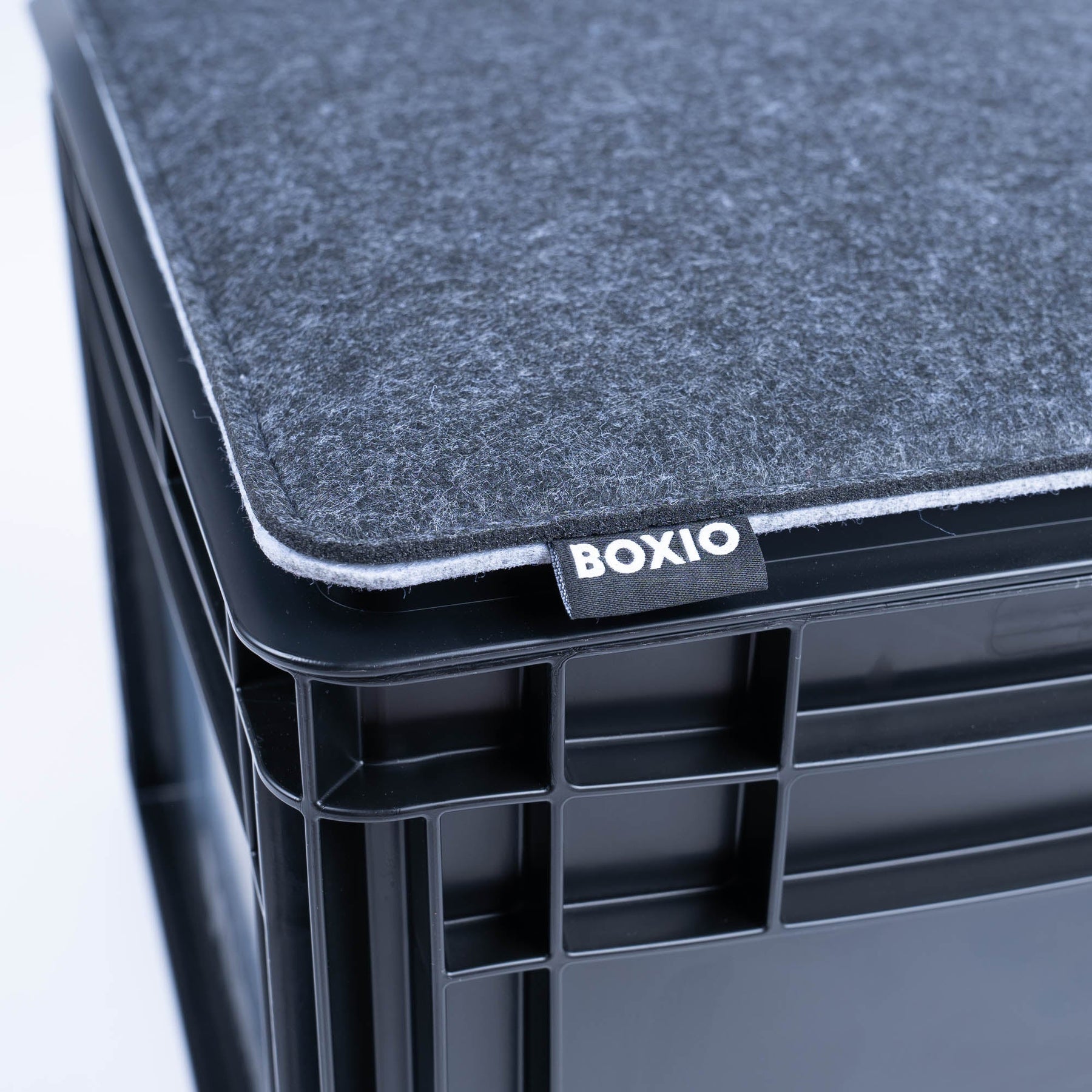 Graues BOXIO SIT Sitzkissen auf schwarzer Eurobox mit sichtbarer BOXIO-Labelnaht und abgerundeter Kante, nah aufgenommen