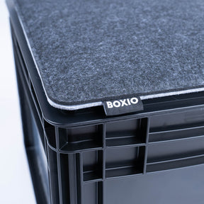 Graues BOXIO SIT Sitzkissen auf schwarzer Eurobox mit sichtbarer BOXIO-Labelnaht und abgerundeter Kante, nah aufgenommen