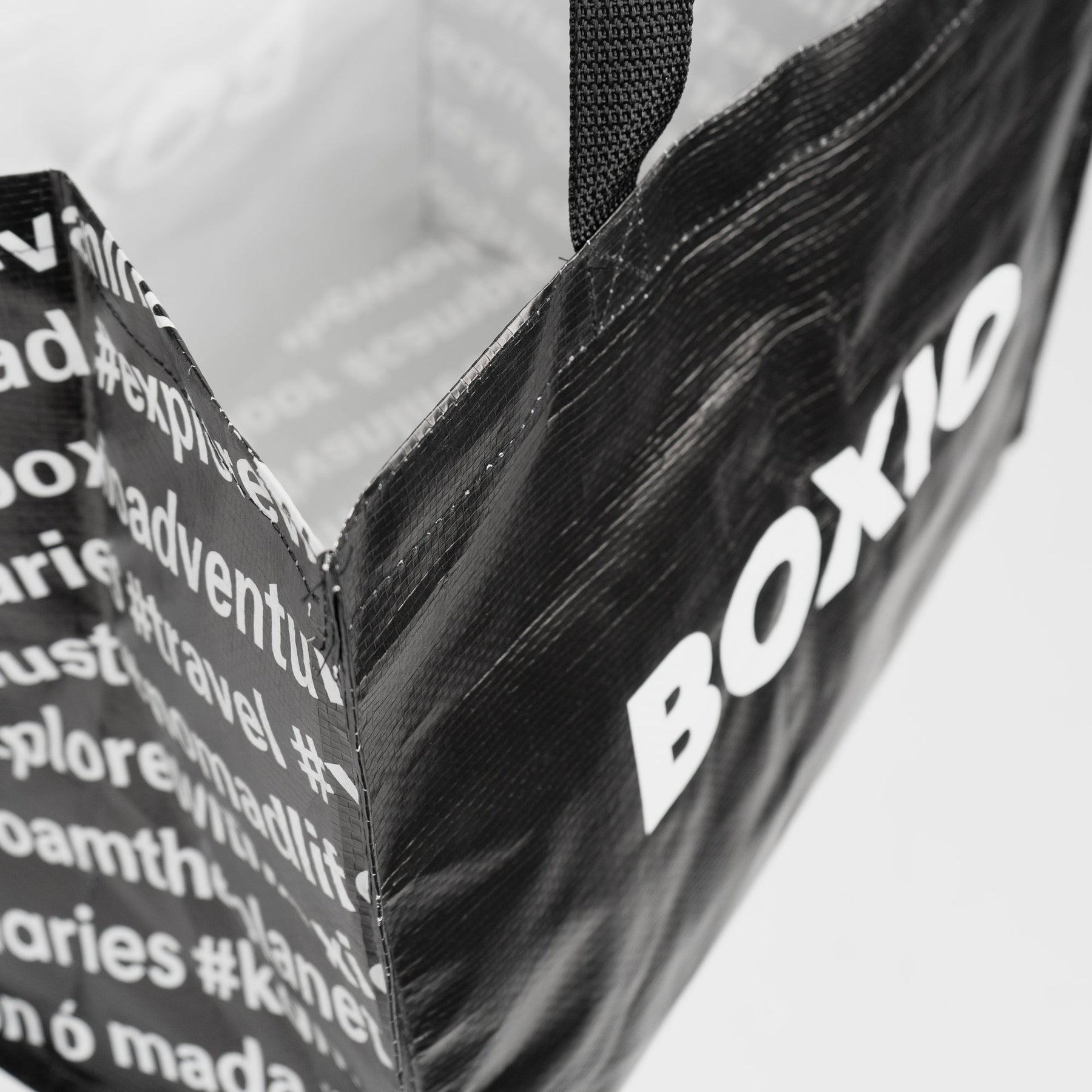 Schwarze BOXIO BAG Tragetasche mit gewebtem Henkel und weißem Logo sowie Schriftzug aus Recyclingmaterial, nah aufgenommen