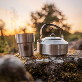 Camping-Kochset BOXIO COOK MAX+ aus Edelstahl mit Kessel und Becher auf moosigem Felsen im Sonnenuntergang