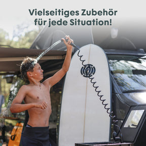 Junge duscht sich mit Handbrause am BOXIO WASH MAX+ neben Surfbrett und Campervan, Wasser spritzt, Text: Vielseitiges Zubehör für jede Situation!