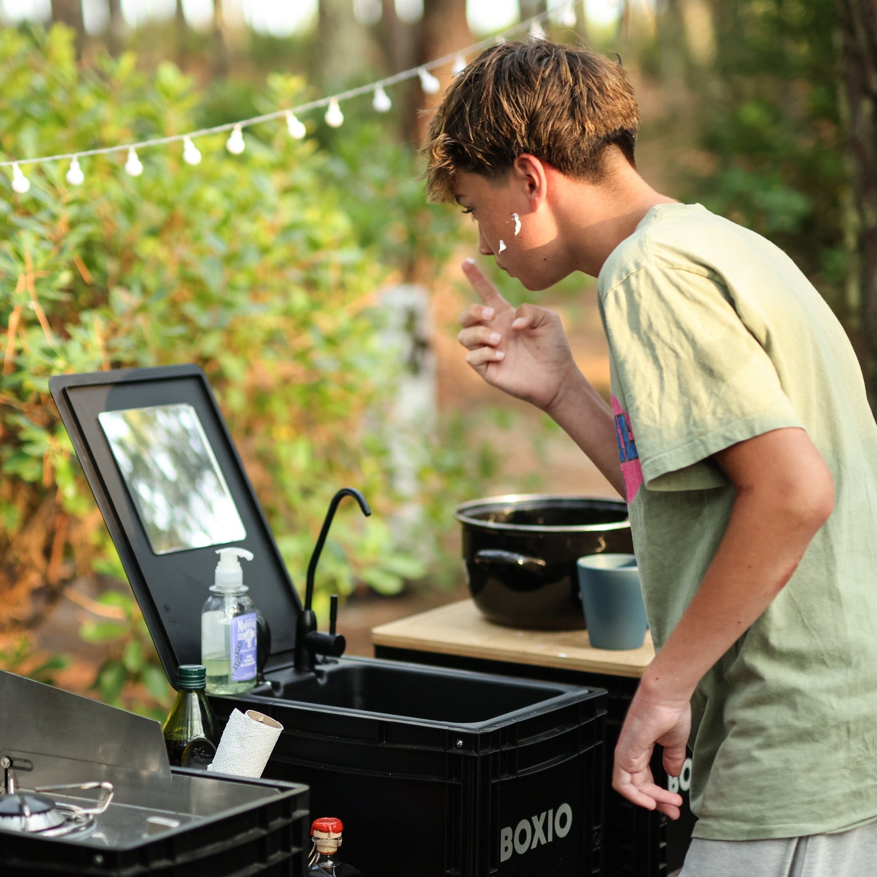 Junger Mann nutzt BOXIO WASH MAX+ Camping Waschbecken mit Spiegel, Wasserhahn und Seife beim Waschen im Freien